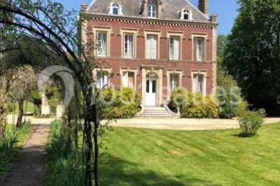 Glycine en fleurs grimpant sur une pergola, avec une maison en briques et des arbustes en arrière-plan.