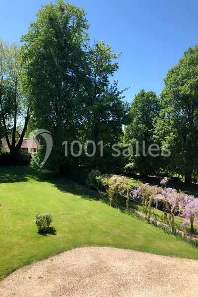 Vue d'un jardin avec pelouse, arbres feuillus et pergola couverte de glycines sous un ciel bleu clair.