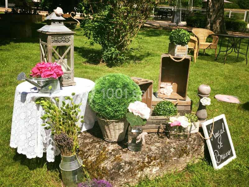 Décoration champêtre avec fleurs, lanternes et caisses en bois disposées sur une souche dans un jardin verdoyant.