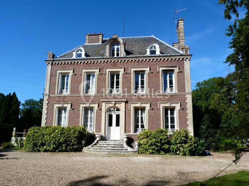 Façade d'une maison en briques rouges avec toit en ardoise, entourée de verdure et d'une allée gravillonnée.