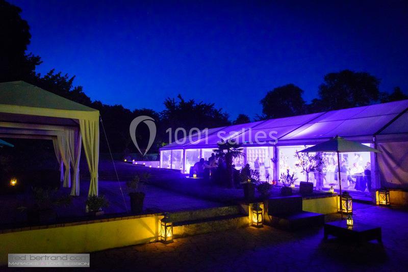Tente éclairée en violet dans un jardin nocturne, entourée de lanternes et de végétation.