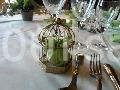 Petit cadeau emballé dans une cage dorée décorative, posé sur une table dressée avec couverts et verres.