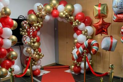 Arche décorative en ballons rouges, blancs et dorés avec cannes en sucre, entourée de rubans et de ballons étoilés.