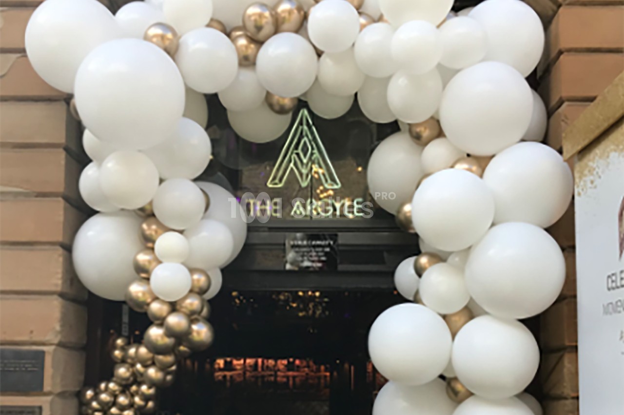 Entrée décorée d'arcs de ballons blancs et dorés, avec une enseigne lumineuse affichant ’The Argyle’.