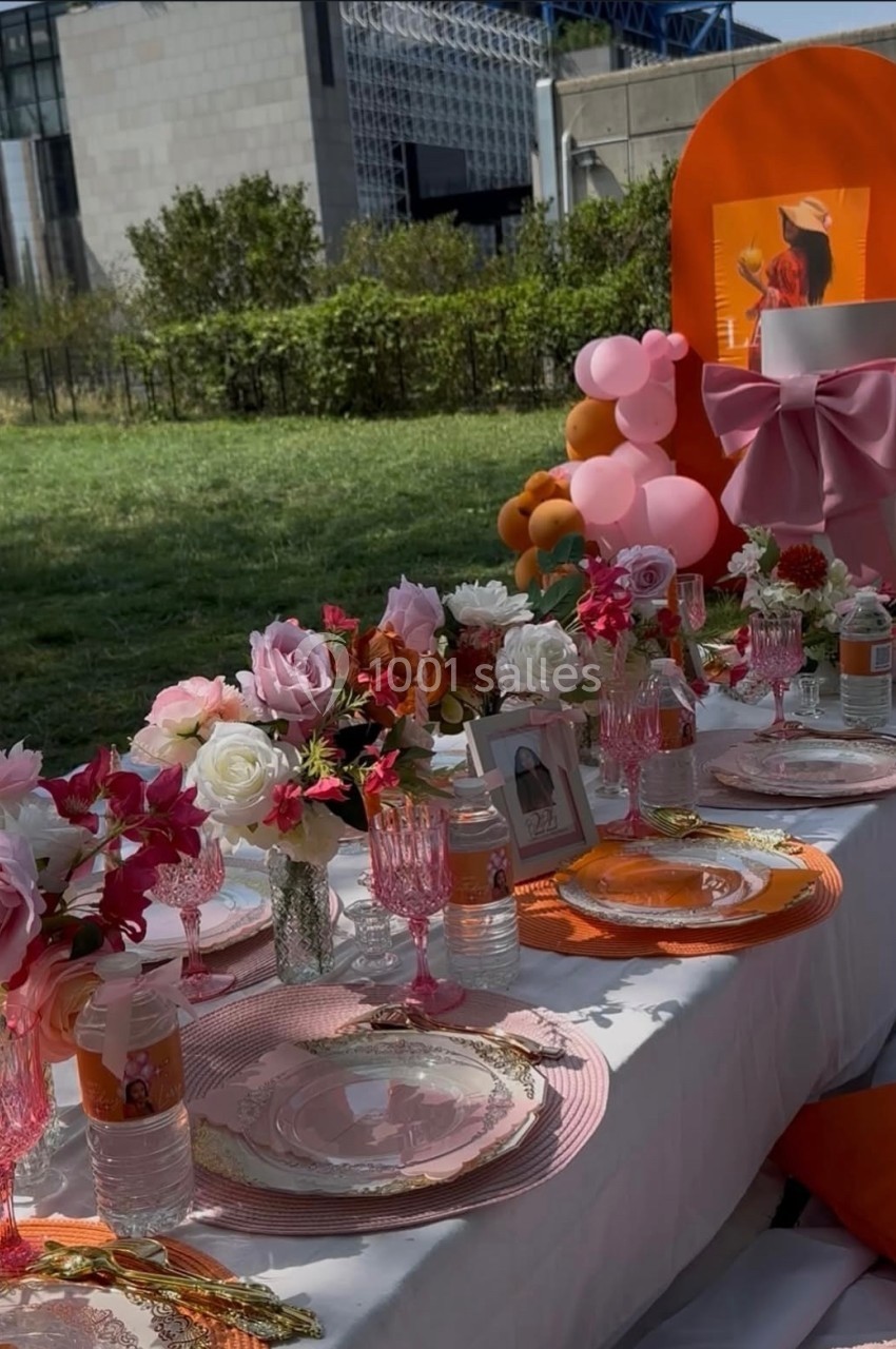 Table décorée en extérieur avec vaisselle élégante, fleurs roses, ballons colorés et éléments décoratifs orange.