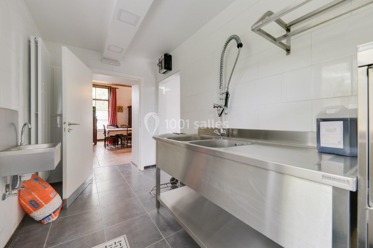 Cuisine professionnelle avec évier en inox, robinet flexible, carrelage gris au sol et vue sur une pièce adjacente.