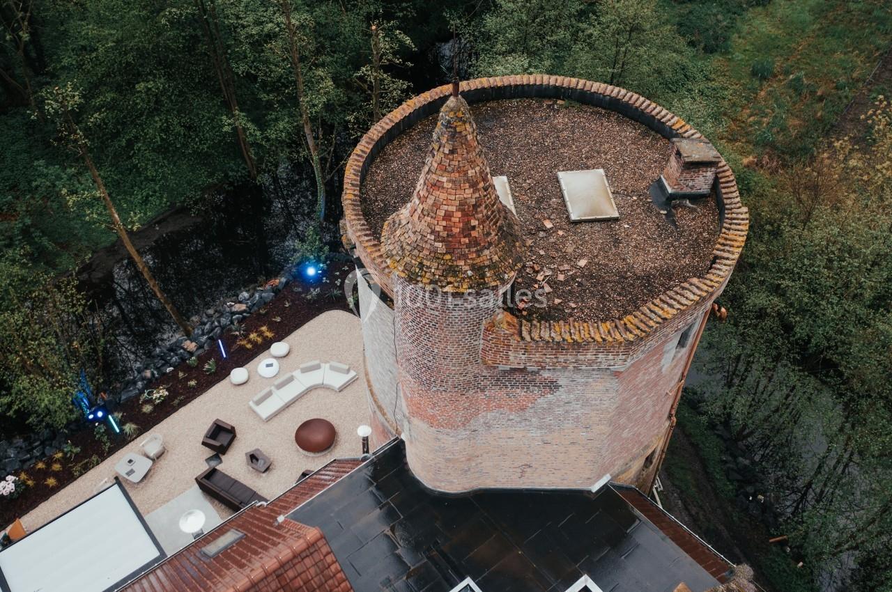 Vue aérienne d'une tour en briques avec un toit conique, entourée de végétation et d'une terrasse aménagée.
