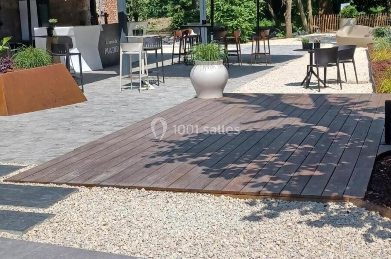 Terrasse extérieure avec tables, chaises, parasols noirs et végétation environnante sous un ciel dégagé.