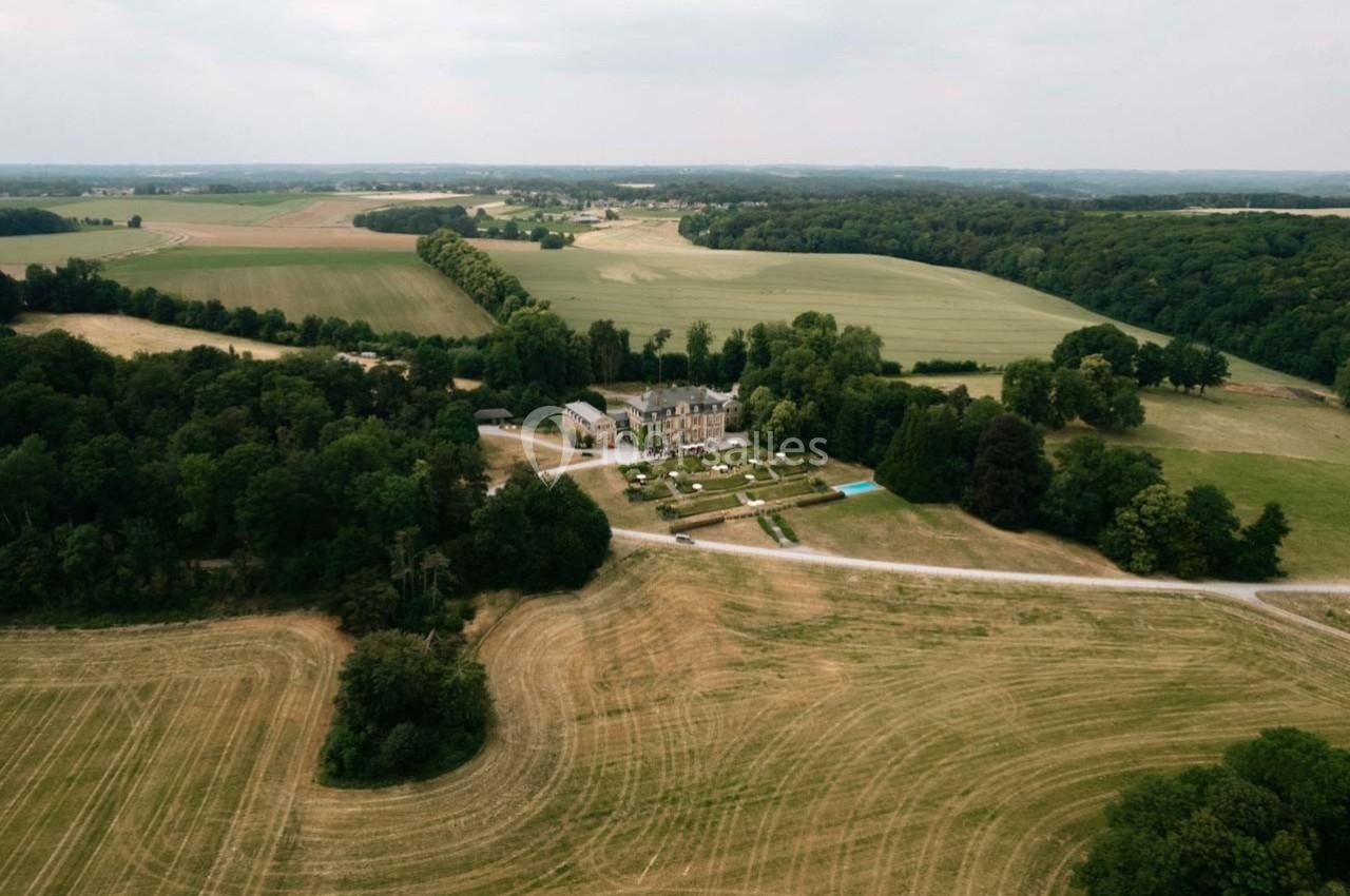 Vue aérienne d'un domaine entouré de champs et de forêts sous un ciel légèrement couvert.