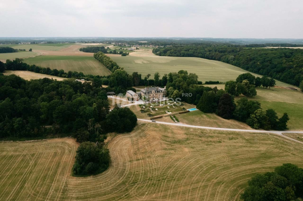 Vue aérienne d'un domaine entouré de champs et de forêts sous un ciel légèrement couvert.