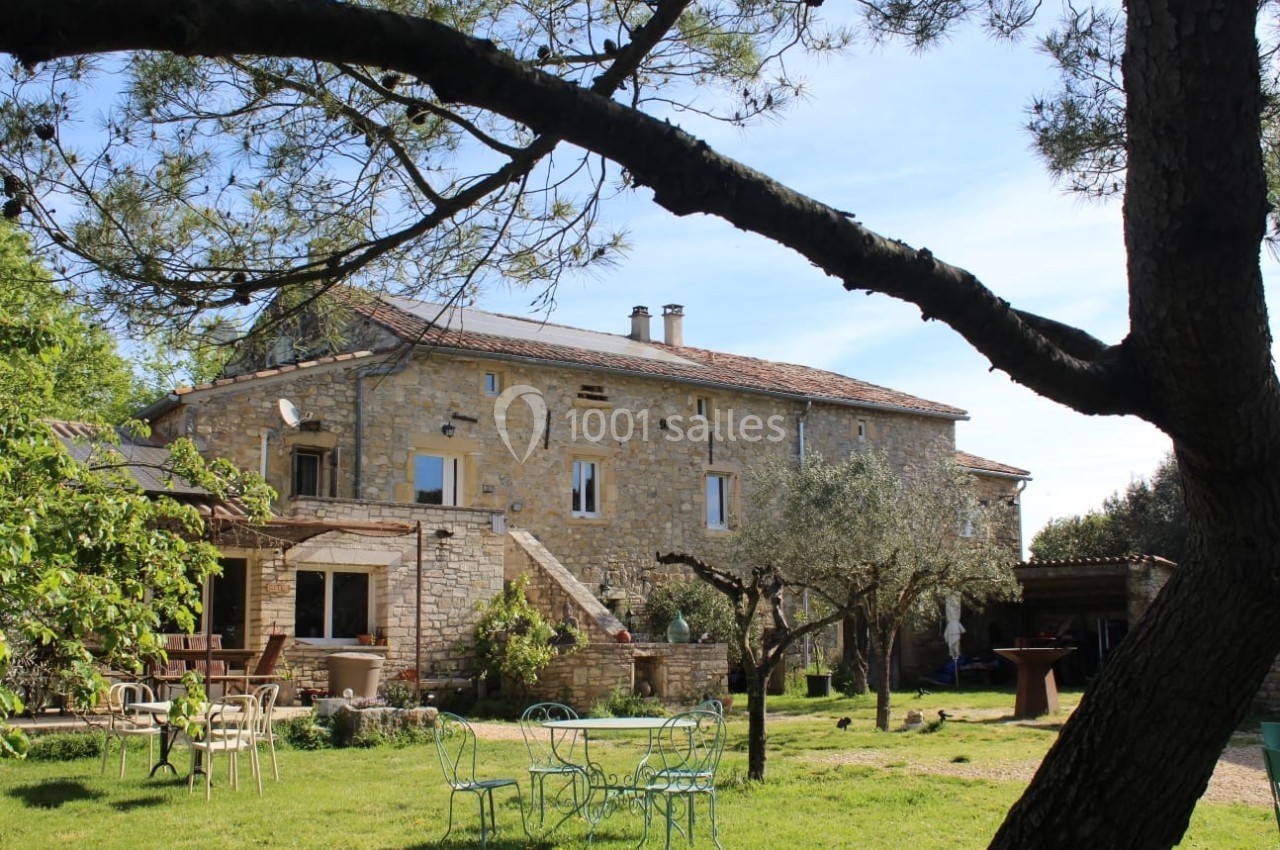 Bâtisse en pierre entourée d'arbres, avec mobilier de jardin sur une pelouse sous un ciel dégagé.