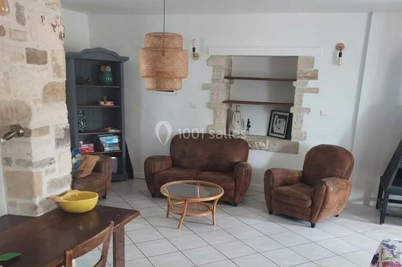 Salon lumineux avec murs en pierre, mobilier vintage en cuir, étagères intégrées et suspension en osier.
