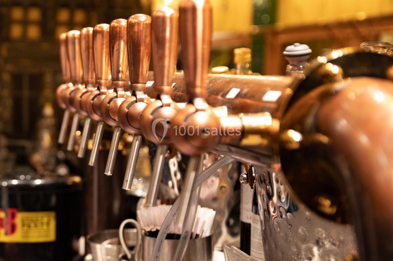 Robinetterie en cuivre alignée sur un comptoir, utilisée pour le service de boissons dans un bar ou une brasserie.