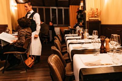Salle de restaurant avec tables dressées, banquettes en bois, bar en bois et étagères garnies de verres et bouteilles.