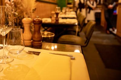 Salle de restaurant avec tables dressées, banquettes en bois, bar en bois et étagères garnies de verres et bouteilles.
