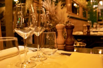 Salle de restaurant avec tables dressées, banquettes en bois, bar en bois et étagères garnies de verres et bouteilles.