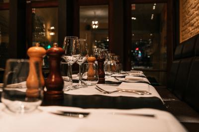 Salle de restaurant avec tables dressées, banquettes en bois, bar en bois et étagères garnies de verres et bouteilles.