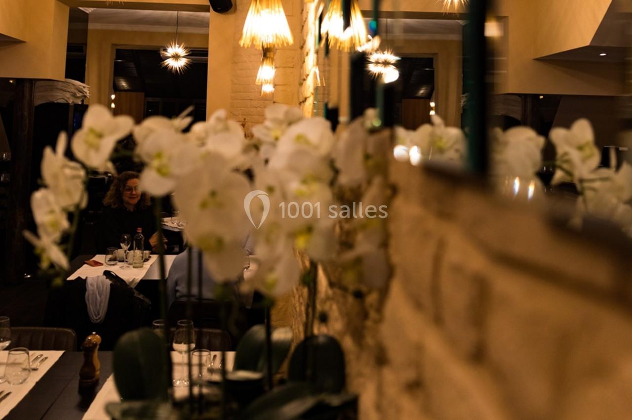 Fleurs blanches d'orchidées au premier plan dans un restaurant à l'éclairage tamisé avec des tables dressées.