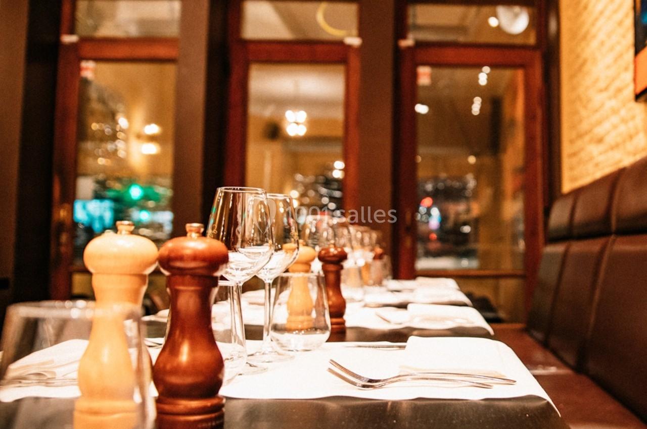 Tables dressées avec verres, couverts et moulins à épices dans un restaurant à l'ambiance chaleureuse et éclairage tamisé.