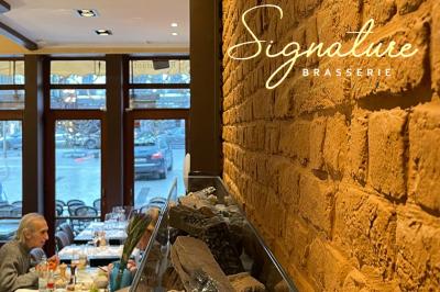 Salle de restaurant avec tables dressées, banquettes en bois, bar en bois et étagères garnies de verres et bouteilles.