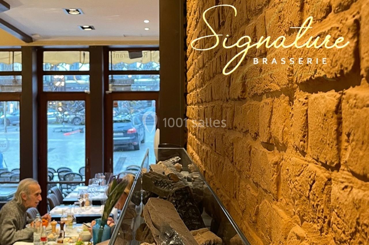 Mur en briques avec des tables dressées dans une brasserie lumineuse, vue sur des fenêtres donnant sur la rue.