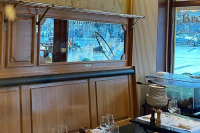Salle de restaurant avec tables dressées, banquettes en bois, bar en bois et étagères garnies de verres et bouteilles.