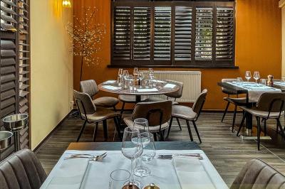 Salle de restaurant avec tables dressées, banquettes en bois, bar en bois et étagères garnies de verres et bouteilles.