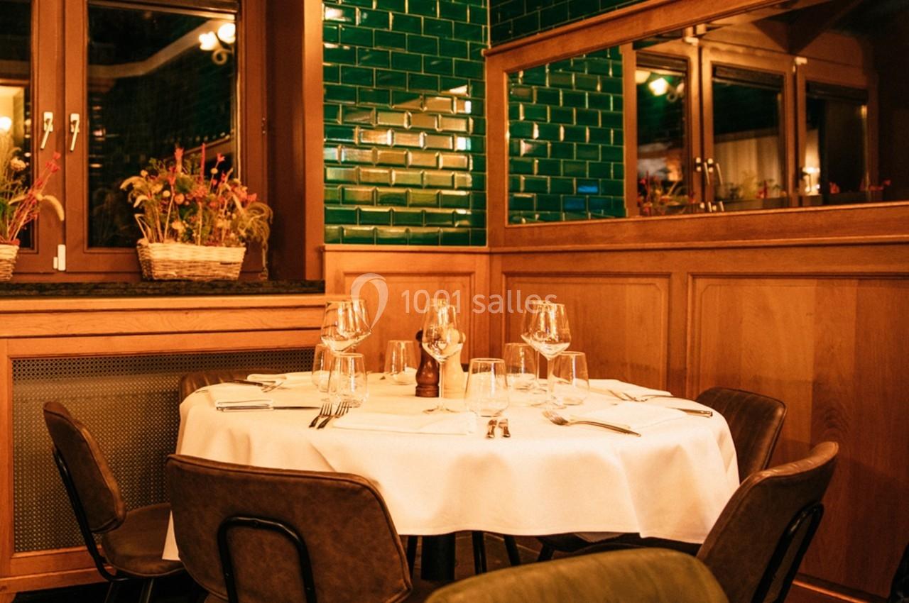 Table dressée avec nappes blanches, verres et couverts dans un restaurant à la décoration boisée et carrelage vert.