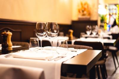 Salle de restaurant avec tables dressées, banquettes en bois, bar en bois et étagères garnies de verres et bouteilles.