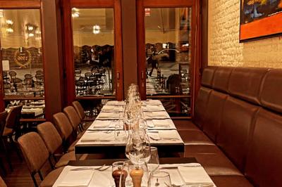 Salle de restaurant avec tables dressées, banquettes en bois, bar en bois et étagères garnies de verres et bouteilles.
