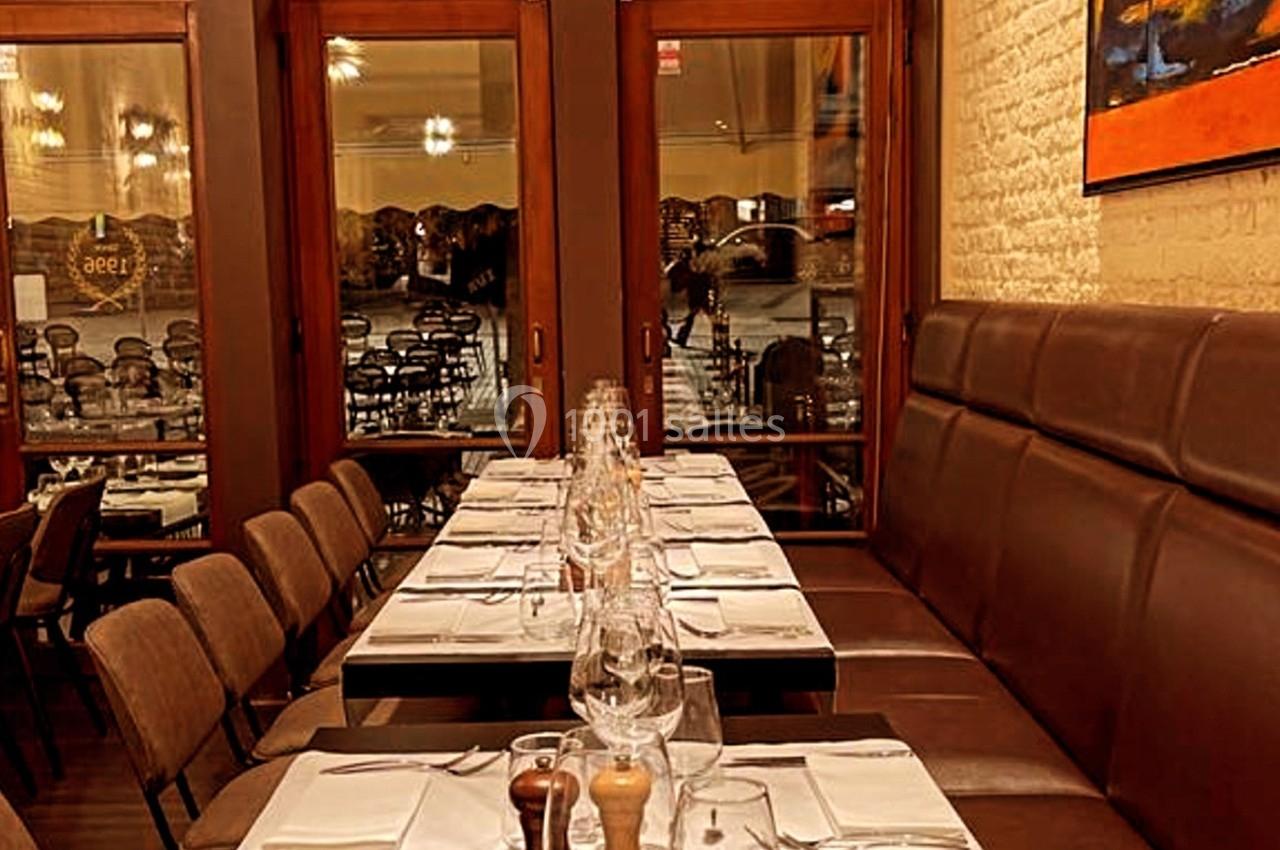 Salle de restaurant avec tables dressées, nappes blanches, chaises en bois et banquettes, éclairage chaleureux.