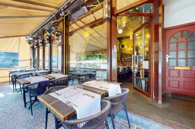 Salle de restaurant avec tables dressées, banquettes en bois, bar en bois et étagères garnies de verres et bouteilles.