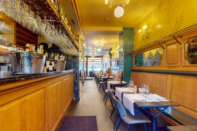 Salle de restaurant avec tables dressées, banquettes en bois, bar en bois et étagères garnies de verres et bouteilles.