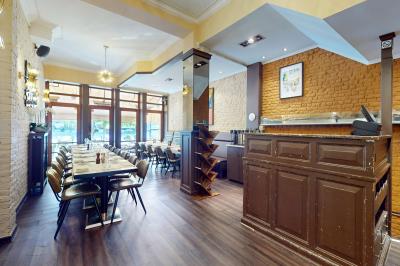 Salle de restaurant avec tables dressées, banquettes en bois, bar en bois et étagères garnies de verres et bouteilles.