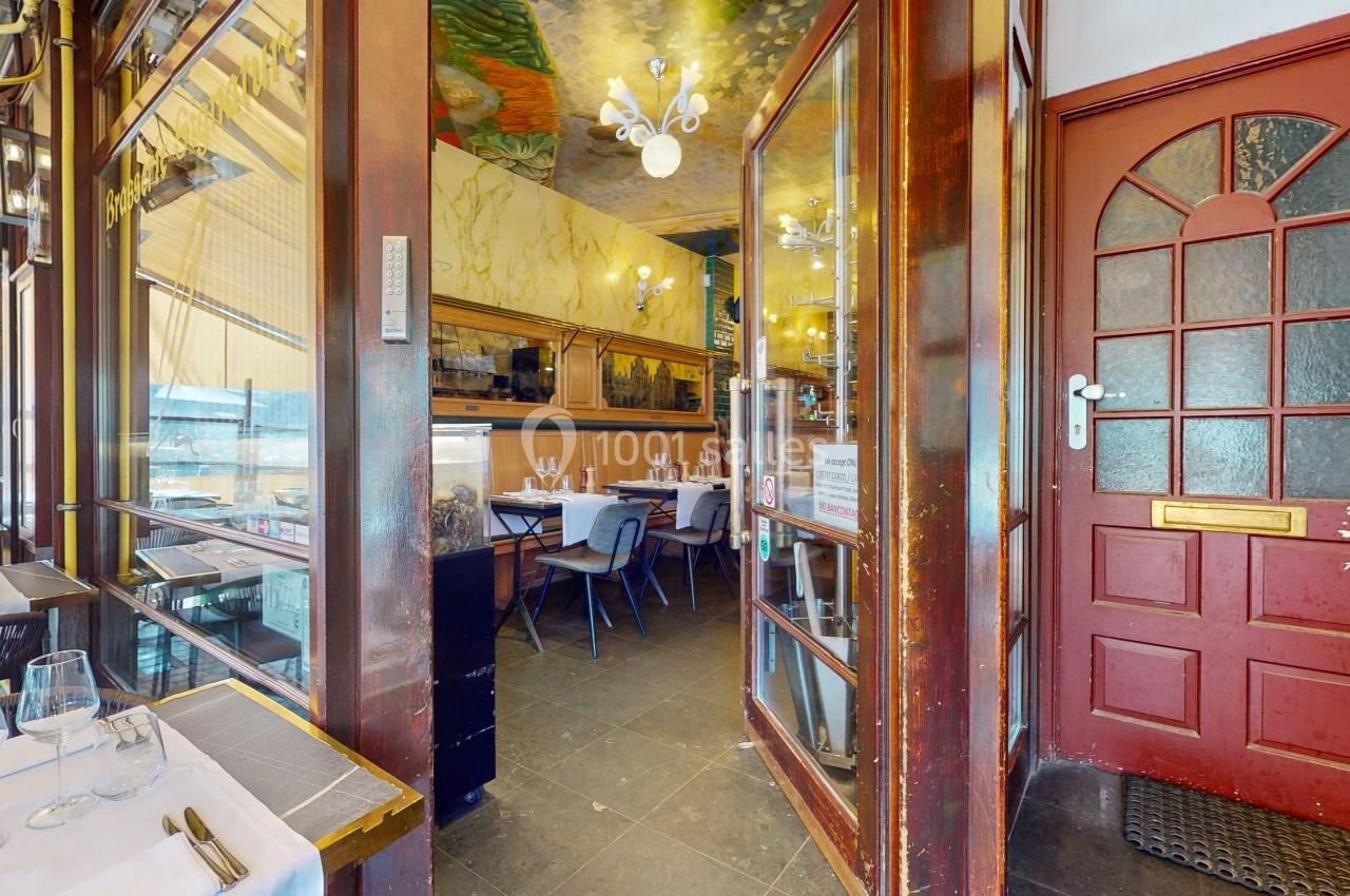 Entrée d'un restaurant avec une salle lumineuse, des tables dressées et un plafond décoré.