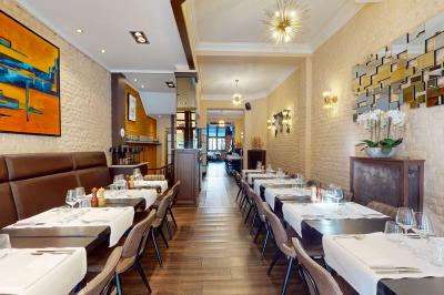 Salle de restaurant avec tables dressées, banquettes en bois, bar en bois et étagères garnies de verres et bouteilles.