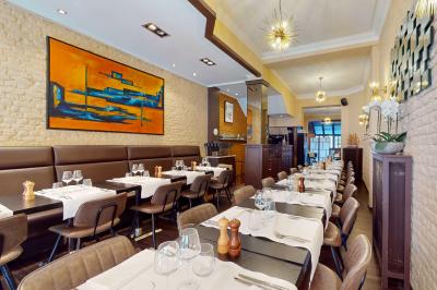Salle de restaurant avec tables dressées, banquettes en bois, bar en bois et étagères garnies de verres et bouteilles.