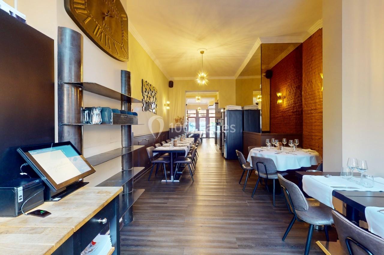 Salle de restaurant lumineuse avec tables dressées, murs en briques et horloge murale décorative.