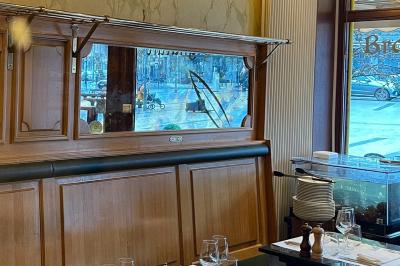 Salle de restaurant avec tables dressées, banquettes en bois, bar en bois et étagères garnies de verres et bouteilles.