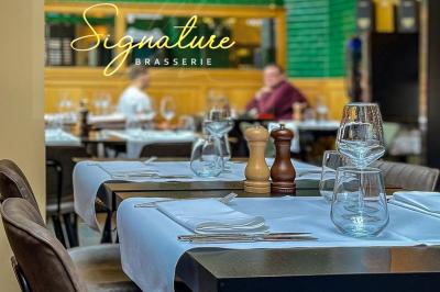 Salle de restaurant avec tables dressées, banquettes en bois, bar en bois et étagères garnies de verres et bouteilles.