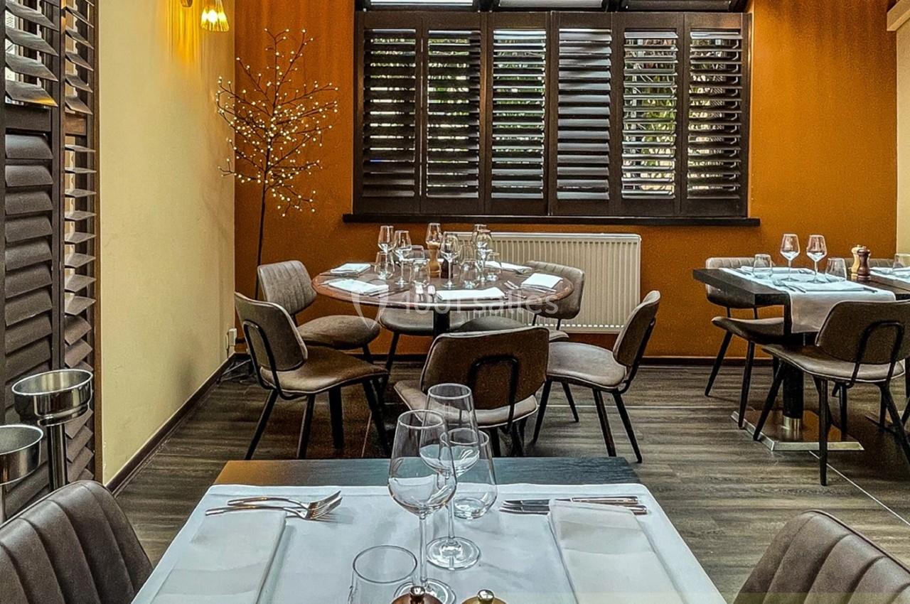 Salle de restaurant moderne avec tables dressées, chaises rembourrées et lumière naturelle filtrée par des volets en bois.