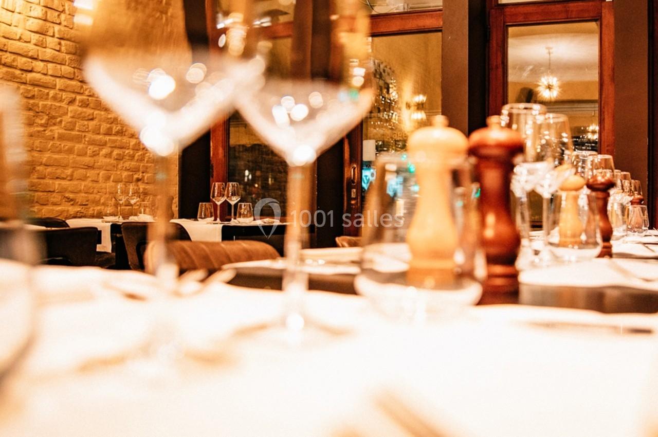 Table dressée dans un restaurant avec verres, couverts et moulins à épices, éclairage chaleureux en arrière-plan.