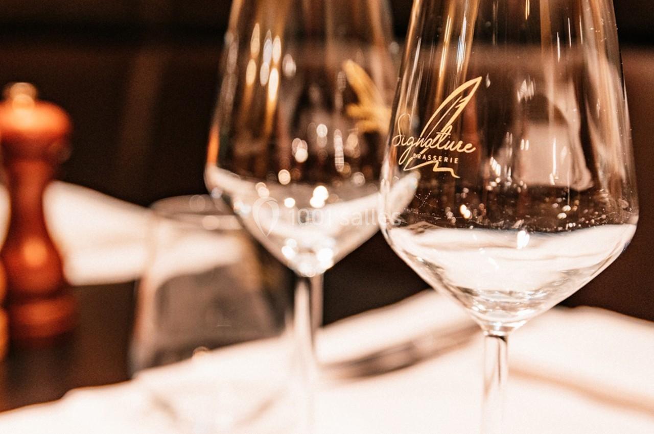 Deux verres à vin transparents posés sur une table dressée avec un moulin à poivre en arrière-plan flou.