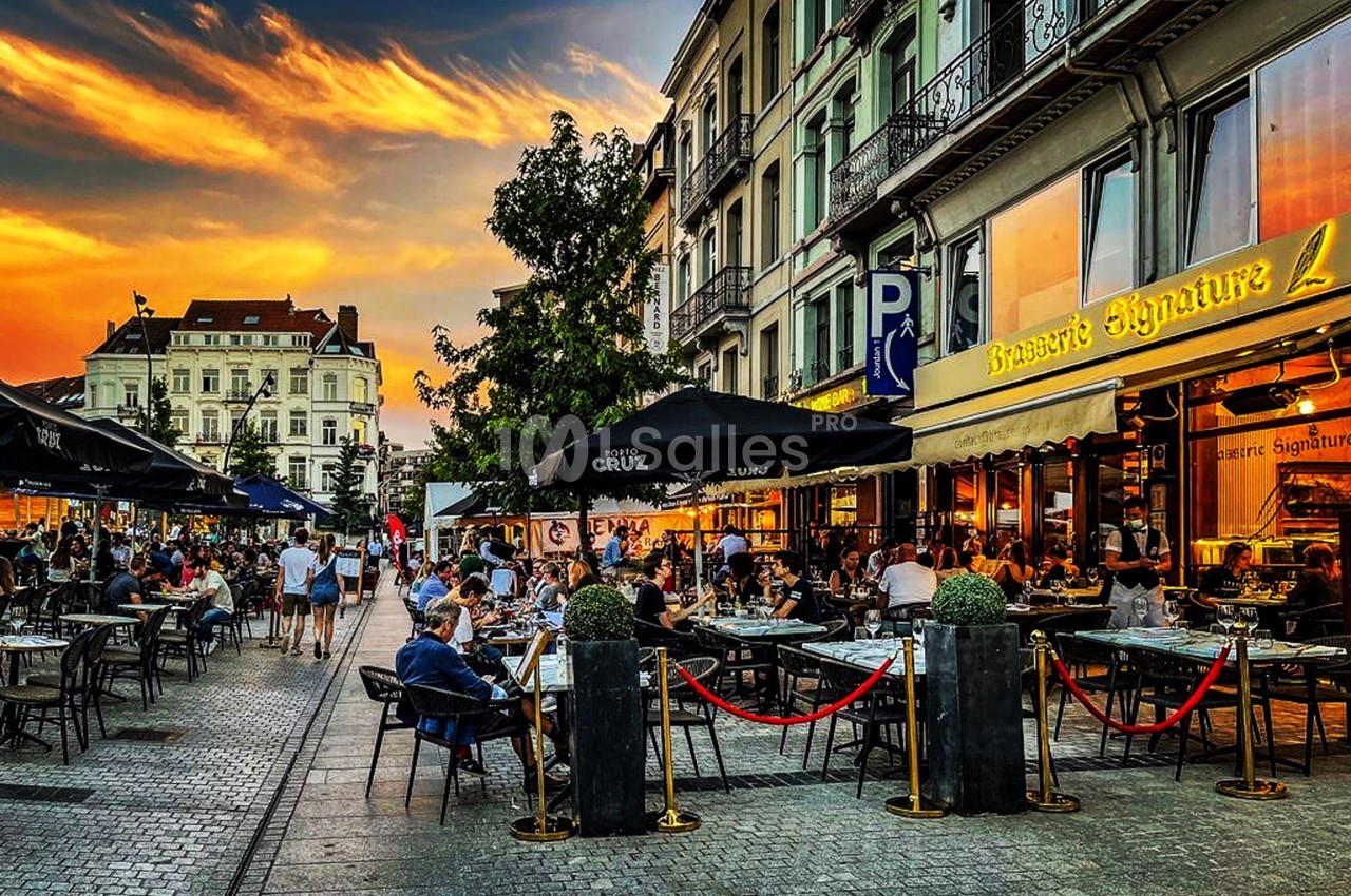 Terrasse animée d'un restaurant en soirée, avec des clients attablés sous un ciel coloré au coucher du soleil.