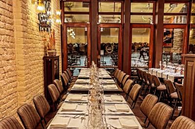 Salle de restaurant avec tables dressées, banquettes en bois, bar en bois et étagères garnies de verres et bouteilles.