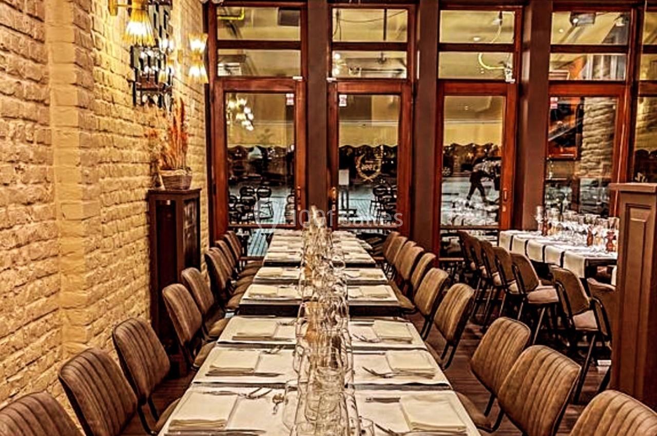 Salle de restaurant élégante avec une longue table dressée, entourée de chaises, et des baies vitrées en arrière-plan.