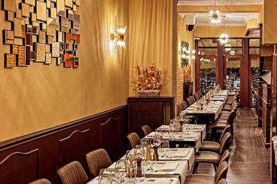 Salle de restaurant avec tables dressées, banquettes en bois, bar en bois et étagères garnies de verres et bouteilles.
