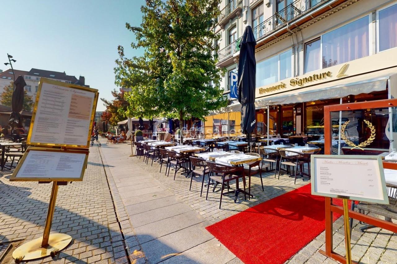 Terrasse d'un restaurant avec tables dressées, menus affichés à l'entrée et un tapis rouge sur le trottoir.