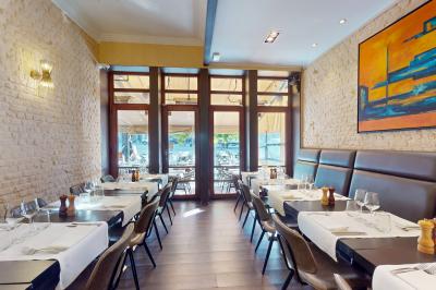 Salle de restaurant avec tables dressées, banquettes en bois, bar en bois et étagères garnies de verres et bouteilles.