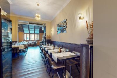 Salle de restaurant avec tables dressées, banquettes en bois, bar en bois et étagères garnies de verres et bouteilles.
